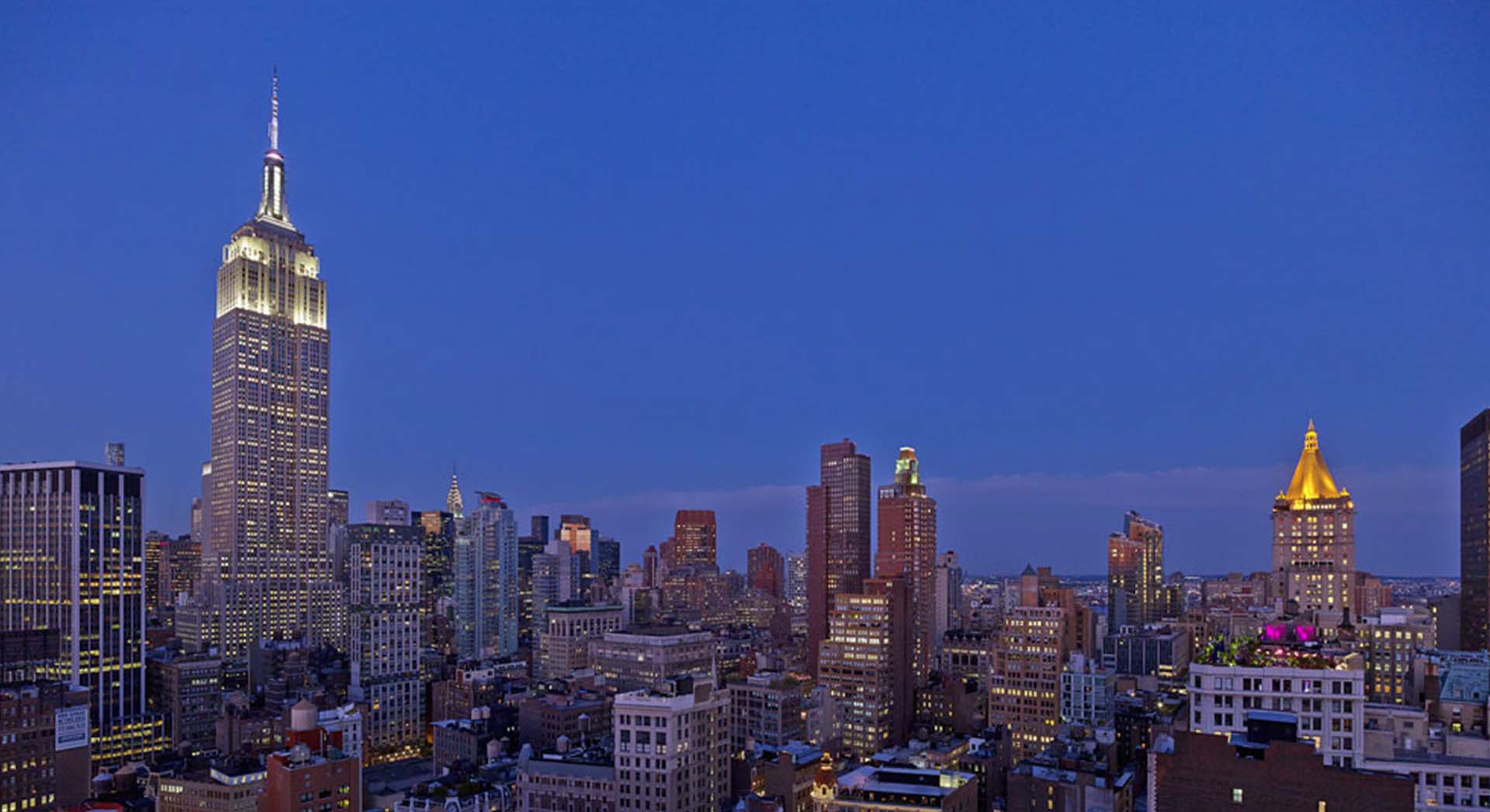 View of the manhattan skyline at dusk with the empire state building illuminated in white