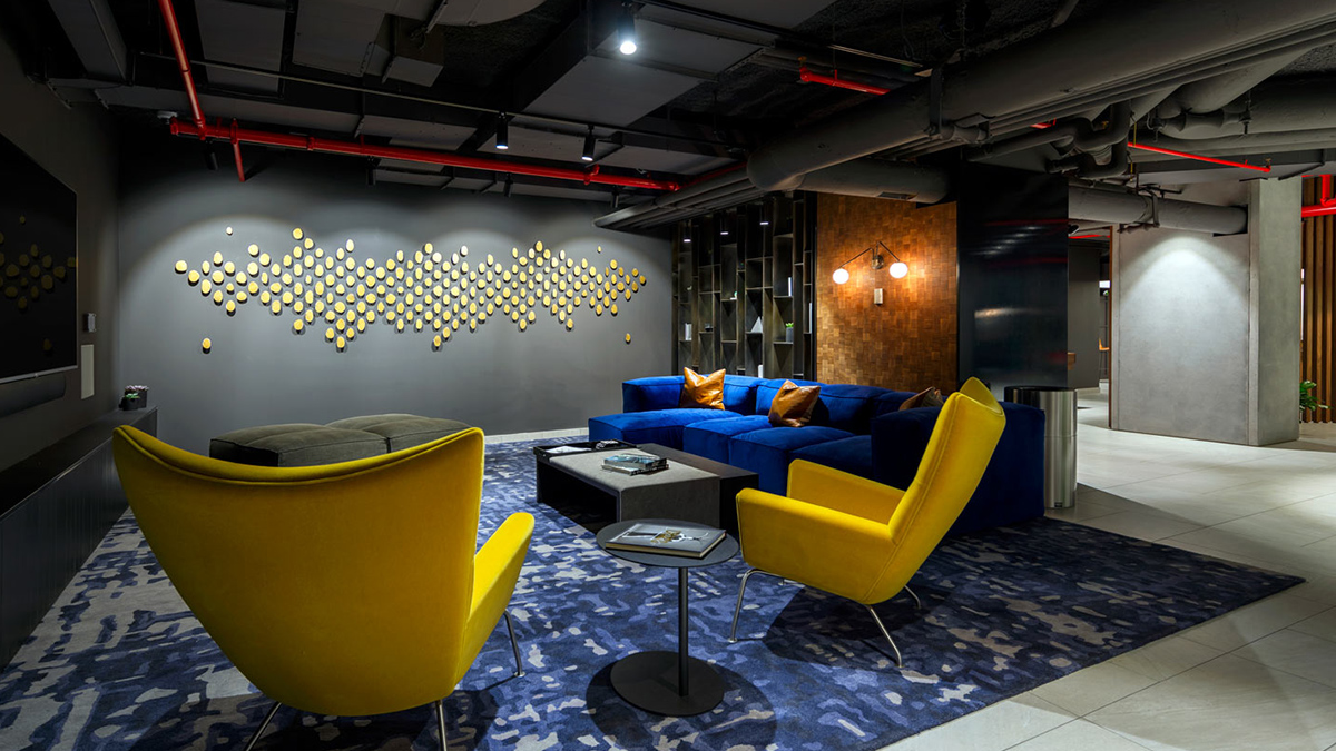 Lounge with modern art on wall, large yellow chairs and blue couch in velvet finish